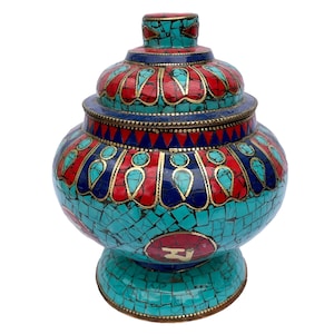 May include: A decorative lidded jar featuring an intricate mosaic pattern of turquoise, red, and dark blue stone inlays set in metal. The body displays a central red circular medallion with a white symbol, surrounded by geometric petal motifs.
