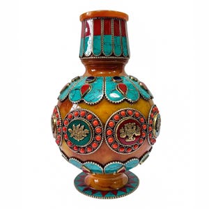 May include: A decorative vase with a rounded body and a narrow neck, featuring a warm amber-colored base. The surface is adorned with inlaid turquoise-colored stone segments, vibrant orange bead accents, and circular medallions with gold-toned relief motifs.
