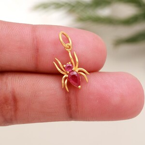 Puede incluir: Un dije de araña de color dorado con un lazo para un collar o pulsera. La araña tiene una cabeza de piedra preciosa rosa redonda y un cuerpo de piedra preciosa rosa en forma de pera. Las patas de la araña son finas y curvas.