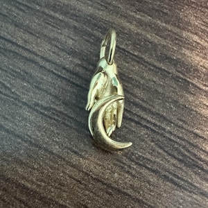 May include: A gold-toned metal pendant shaped like a hand holding a crescent moon. The pendant features a small loop at the top for attachment, with a polished finish that reflects light across the detailed contours of the fingers and the moon.