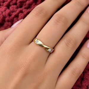 Op de afbeelding: Een gouden bandring met een gedraaid ontwerp en twee kleine, heldere, rond geslepen stenen die in het metaal zijn gezet. De ring heeft een gepolijste afwerking en een doorlopende, vloeiende vorm die een subtiel spiraaleffect op de band creëert.