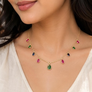 May include: A gold chain necklace featuring multiple teardrop-shaped gemstones in vibrant shades of pink, green, and blue. The stones are evenly spaced along the delicate metal links, creating a colorful and symmetrical arrangement around the neck.