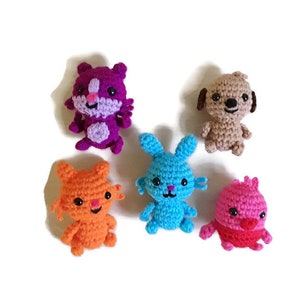 May include: A collection of five small crocheted animal figures including a purple squirrel, a tan dog, an orange cat, a bright blue rabbit, and a pink bird. Each figure features black bead eyes and detailed yarn stitching in vibrant colors.
