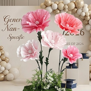 May include: A display of large, paper flowers in shades of pink and white, arranged with greenery. The backdrop features text that reads "Gener Nan-Specific" and "Class of 2026". Graduation caps and books are also visible.