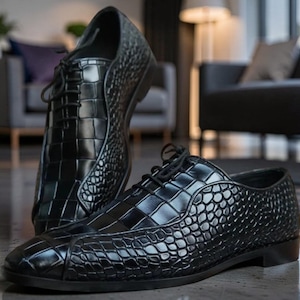 Può includere: Un paio di scarpe stringate nere con finitura lucida, caratterizzate da una combinazione di texture goffrate rettangolari grandi e arrotondate più piccole sulla tomaia, lacci neri sottili e un tacco basso su una suola scura e liscia.