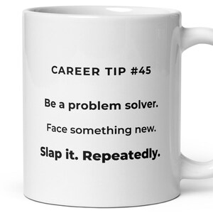 May include: White ceramic mug with the text "CAREER TIP #45" and the advice "Be a problem solver. Face something new. Slap it. Repeatedly." The mug has a curved handle.