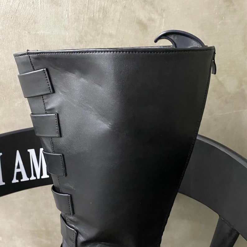 May include: Black leather knee-high boots with a zipper on the back and multiple straps on the side.