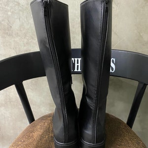 May include: A pair of black leather knee-high boots with a zipper on the back of each boot.