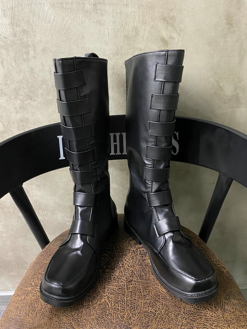 May include: A pair of black leather knee-high boots with a buckle strap detail on the back of the shaft. The boots have a pointed toe and a low heel.