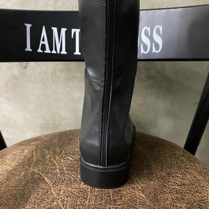 May include: Black leather knee-high boots with a zipper up the back. The boots have a rounded toe and a flat heel.