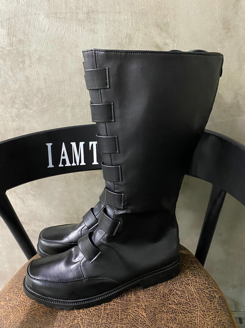 May include: Black leather boots with a buckle strap design. The boots have a tall shaft and a rounded toe.