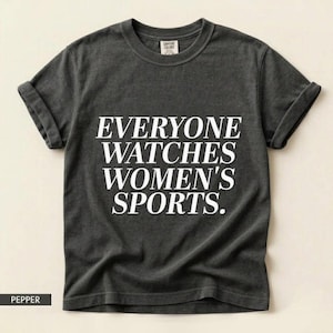 Könnte beinhalten: Dunkelgraues T-Shirt mit hochgekrempelten Ärmeln. Der Text "EVERYONE WATCHES WOMEN'S SPORTS" ist in weißen Buchstaben aufgedruckt. Unten ist das T-Shirt mit "PEPPER" beschriftet.