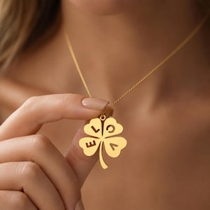 Può includere: Una collana color oro con un ciondolo a forma di quadrifoglio. Il quadrifoglio è caratterizzato da lettere ritagliate che compongono la parola LOVE, con una lettera posizionata su ciascuna delle quattro foglie. Il ciondolo pende da una sottile catenina.