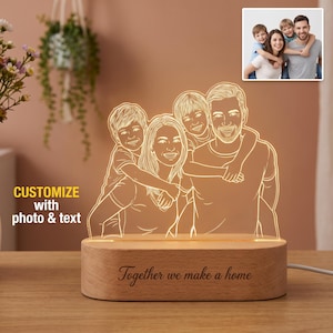 May include: A custom LED night light featuring an acrylic panel with an engraved family portrait based on a photo, illuminated in warm light. The light sits on a smooth oval wooden base with the engraved text Together we make a home.