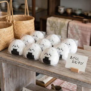 Puede incluir: Una exhibici&oacute;n de onigiri con forma de foca, bolas de arroz japonesas, con algas nori y caras adorables. Las bolas de arroz est&aacute;n envueltas individualmente y dispuestas sobre una superficie de madera. Tambi&eacute;n hay un letrero con texto japon&eacute;s.