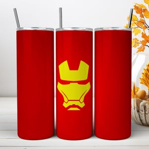 May include: Three tall, cylindrical red tumblers with silver metal straws. The center tumbler features a yellow graphic of a stylized helmet mask. Each tumbler has a flat lid and a smooth, solid red finish, providing a consistent look across all items.