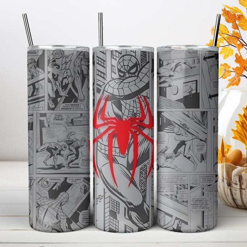 Puede incluir: Un vaso cil&iacute;ndrico de acero inoxidable con un estampado de c&oacute;mic en blanco y negro que muestra varias escenas de acci&oacute;n y un gran emblema de ara&ntilde;a roja prominente centrado en el frente. El vaso incluye una pajita negra fina en la parte superior.