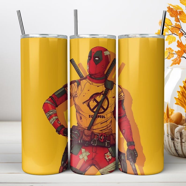 May include: A cylindrical stainless steel tumbler with a yellow background featuring a graphic illustration of the character Deadpool wearing a red mask and a yellow t-shirt with a black logo. The tumbler includes a metal straw and a lid.
