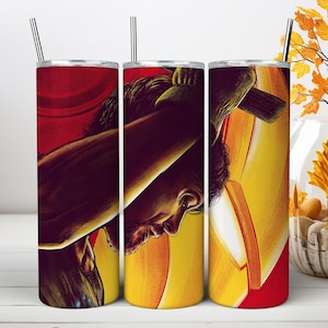 May include: A cylindrical stainless steel tumbler featuring a wrap-around graphic illustration of a person with dark hair holding a large hammer. The design uses a vibrant color palette of deep red, bright yellow, and orange tones with a metal straw.