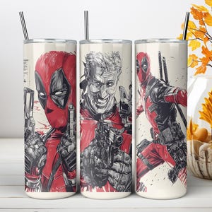 May include: A cylindrical stainless steel tumbler featuring a graphic illustration of the character Deadpool in red and black. The design includes a masked portrait, an unmasked face, and a full-body action pose, each holding a handgun.