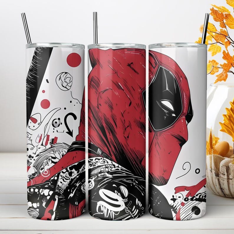 May include: A cylindrical stainless steel tumbler featuring a graphic illustration of a red and black masked character. The design includes abstract black and white line art, red circles, and a metal straw inserted into the top lid of the container.