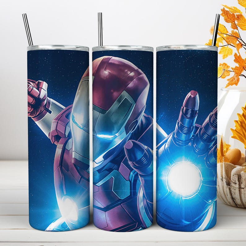 May include: A cylindrical metal tumbler featuring a graphic of a red and gold armored character in a space setting. The character has glowing blue eyes and a bright blue light emanating from the palm of a hand. A thin metal straw is inserted at the top.
