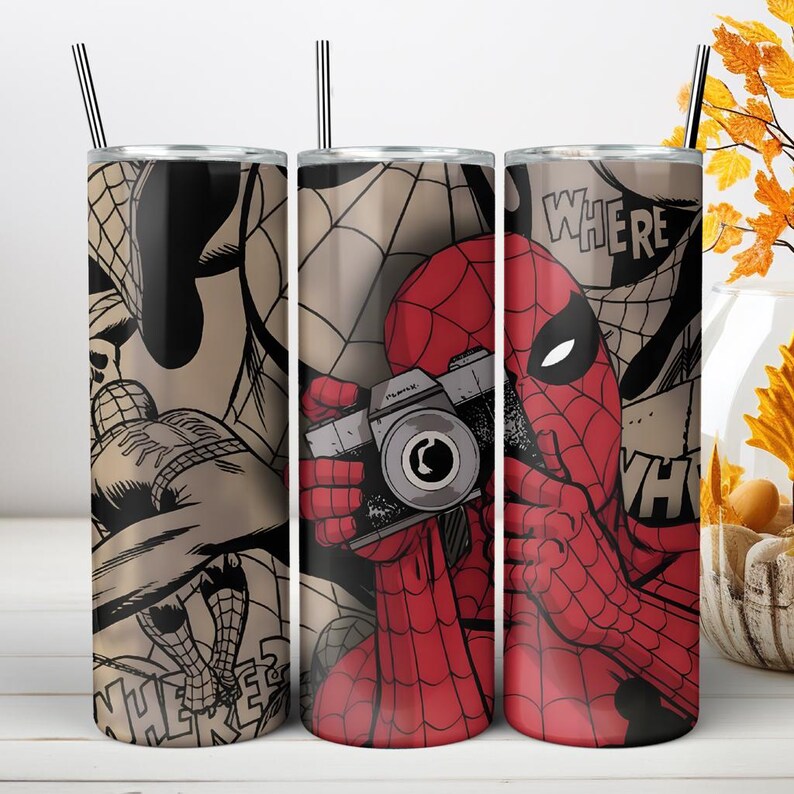 Puede incluir: Un vaso cil&iacute;ndrico con pajita de metal que presenta un gr&aacute;fico de c&oacute;mic de un personaje enmascarado rojo y azul sosteniendo una c&aacute;mara. El dise&ntilde;o incluye patrones de telara&ntilde;a negra y el texto "WHERE" y "WHO" en una fuente de estilo c&oacute;mic.