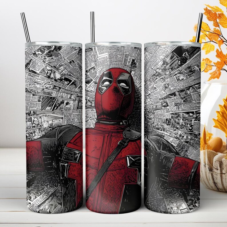 May include: A cylindrical stainless steel tumbler featuring a graphic of the character Deadpool in a red and black suit, set against a background of black and white newspaper clippings. The tumbler includes a thin metal straw inserted at the top.