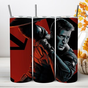 May include: A cylindrical stainless steel tumbler featuring a graphic print of Captain America in a dark blue suit with a red star emblem. The background is a bold red and black geometric design. The tumbler includes a clear lid and a metal straw.