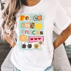 Könnte beinhalten: Weißes T-Shirt mit einem farbenfrohen Grafikdesign. Das Design enthält die Wörter "PEACE SUN SNACKS" in verschiedenen Schriftarten und Farben, zusammen mit Illustrationen einer Sonne, einer Orangenscheibe, Kirschen und einer Gänseblümchen.