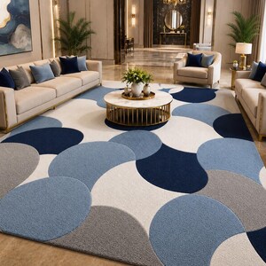 May include: A large area rug featuring a repeating geometric pattern of overlapping circles in shades of navy blue, light blue, gray, and cream. The rug has a textured, plush pile surface and covers the floor space between beige sofas and chairs.