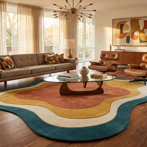 May include: An area rug featuring an organic, wavy shape with concentric layers of color including deep teal, cream, mustard yellow, and burnt orange. The rug is positioned on a wooden floor, showcasing a smooth, solid-colored textile surface.