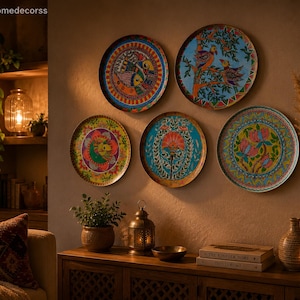 Puede incluir: Cinco platos decorativos de pared con diseños intrincados y coloridos. Los platos presentan motivos florales y de aves en tonos de azul, naranja, verde y amarillo. Los platos están montados en una pared de color neutro, creando una vibrante exhibición de decoración del hogar.