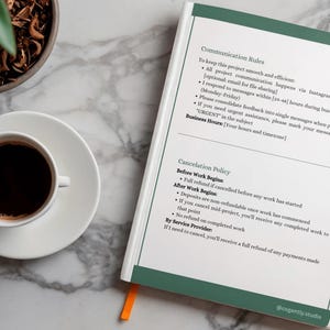 Op de afbeelding: Een witte koffiekop met donkere koffie staat op een witte schotel naast een notitieboek met groene accenten en tekst. Een pen en een kleine potplant staan ook op het marmeren oppervlak.