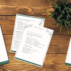May include: A wooden surface displays several white papers with green borders and text. One paper is a branded template, another discusses language positioning, and the third is a project checklist. A small potted plant is in the background.