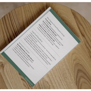 Op de afbeelding: Een boek met een witte kaft en groene rand ligt op een houten tafel. De pagina's van het boek bevatten tekst, waaronder de zinnen "Wat gebeurt er als er iets misgaat?" en "Door de betaling te verzenden, bevestigt u dat u".