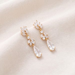 May include: A pair of gold-tone drop earrings featuring a cluster of marquise-cut clear crystals arranged in a leaf-like pattern, terminating in a single pear-shaped crystal drop. The metal setting is polished gold, providing a bright contrast.