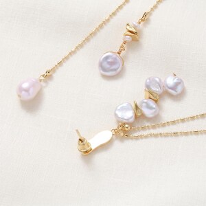 Puede incluir: Juego de joyas doradas con perlas de agua dulce. El conjunto incluye un par de pendientes y dos collares. Los pendientes tienen cierre de poste. Los collares tienen cadenas delicadas y colgantes de perlas. Las perlas son blancas y rosas.