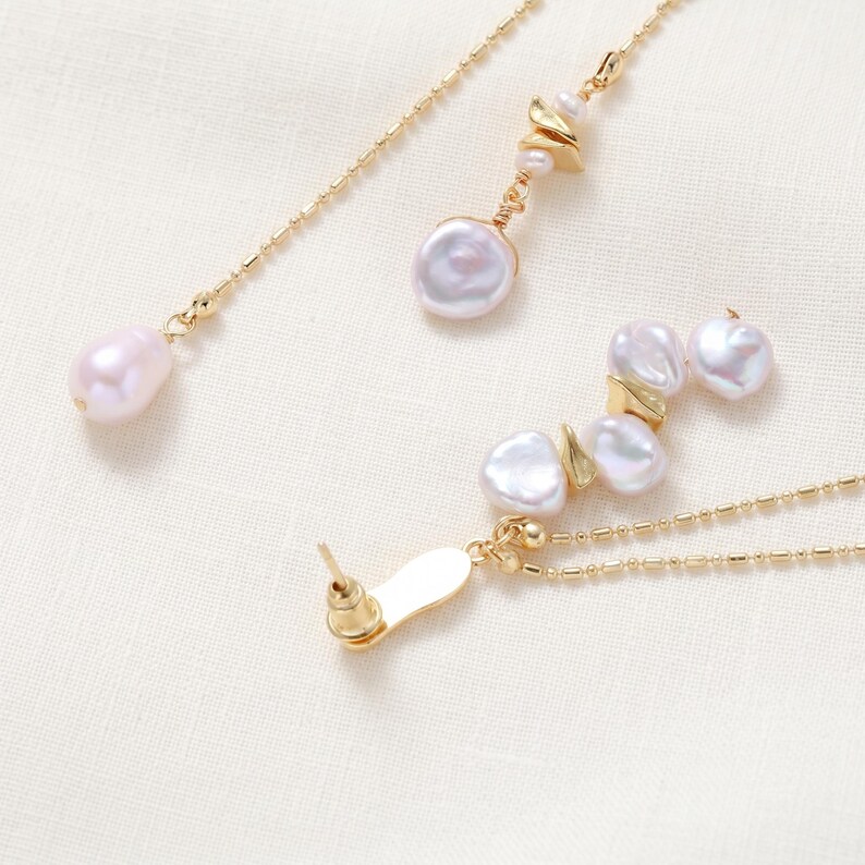Puede incluir: Juego de joyas doradas con perlas de agua dulce. El conjunto incluye un par de pendientes y dos collares. Los pendientes tienen cierre de poste. Los collares tienen cadenas delicadas y colgantes de perlas. Las perlas son blancas y rosas.
