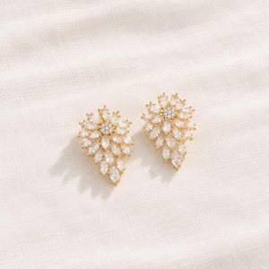 Peut inclure: Une paire de boucles d'oreilles dorées composées d'un groupe de cristaux transparents taille marquise disposés en éventail. Chaque boucle présente un cristal circulaire central entouré de plusieurs couches de pierres pointues en forme de feuille.