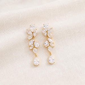 May include: A pair of gold-toned drop earrings featuring a cluster of clear, marquise-cut and pear-shaped cubic zirconia stones arranged in a leaf-like pattern, terminating in a single dangling pear-shaped stone at the base of each earring.