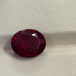 Peut inclure: Une pierre précieuse rouge foncé de taille ovale avec de multiples facettes qui reflètent la lumière. La pierre présente une teinte cramoisie riche et saturée, polie pour obtenir une finition lisse et réfléchissante, révélant sa structure claire.