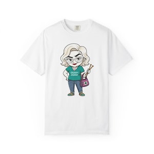 Könnte beinhalten: Ein weißes Kurzarm-T-Shirt mit einer Cartoon-Illustration einer Person mit blonden Haaren, Brille und rotem Lippenstift. Die Figur trägt ein blaugrünes Oberteil mit dem Text GRUMPY GRANNY, eine blaue Jeans und eine lila Tasche mit Stricknadeln.