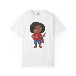 May include: A white t-shirt featuring a cartoon illustration of a person with dark curly hair wearing a red shirt with the text GRUMPY GRANNY, blue jeans, and trainers. The character holds knitting needles and a small patterned bag.