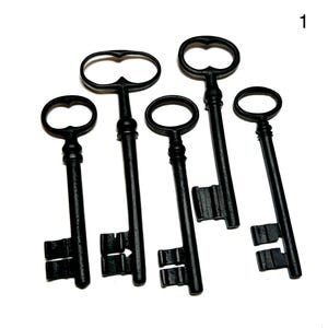 May include: Five black vintage-style keys of varying sizes are arranged on a white surface. Each key has a different handle design, with ornate details and a classic aesthetic. The keys are made of metal.