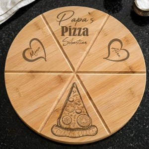 Könnte beinhalten: Rundes Holz-Pizzabrett mit sechs Tortenstücken. Das Brett ist mit "Papa's Pizza Sebastian" graviert und hat herzförmige Designs mit den Namen "Mama" und "Alina". Eine Pizza-Scheiben-Illustration befindet sich in der Mitte.