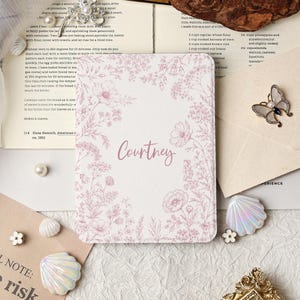 May include: A floral-patterned card with the name "Courtney" in cursive script. The card is surrounded by a delicate pink floral design. Decorative elements include a butterfly brooch, seashells, and pearls.