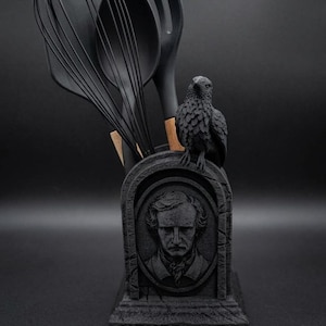 Può includere: Un portautensili da cucina nero a forma di lapide con un ritratto scolpito di Edgar Allan Poe, un corvo appollaiato sopra e la parola NEVERMORE in rilievo alla base. Contiene una frusta, un cucchiaio e un cucchiaio forato di colore nero.