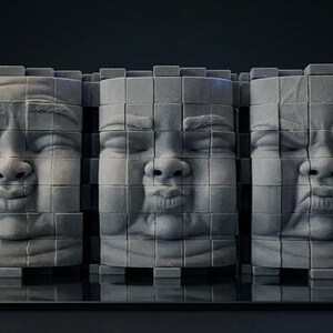 Pode incluir: Três esculturas cilíndricas cinzentas dispostas lado a lado, cada uma composta por uma grelha de pequenos blocos quadrados. Cada escultura apresenta um rosto humano com uma expressão distinta: um sorriso calmo, lábios franzidos e um cenho franzido.
