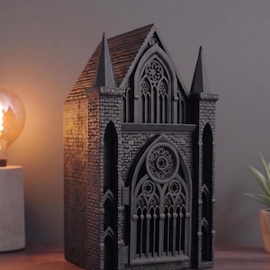 May include: A dark gray, three-dimensional architectural model of a gothic cathedral facade. The structure features intricate brickwork textures, pointed spires, arched windows with detailed tracery, and a prominent circular rose window above the entrance.